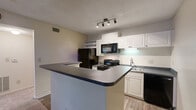 Located at 771 Lindbergh Dr NE in Atlanta's 30324 neighborhood, this one-bedroom, two-bathroom residence is thoughtfully laid out across a single floor. The open-concept kitchen and living area forms the heart of the home, where a wraparound peninsula with a granite-look countertop serves as both a workspace and a casual dining spot. The kitchen is outfitted with white cabinetry, black appliances including an electric range, over-the-range microwave, refrigerator, and dishwasher, along with wood-look flooring and a track lighting fixture overhead. The living area flows naturally from the kitchen and is carpeted for comfort, with French doors that invite natural light and provide access to the outdoors. The bedroom is a well-proportioned retreat featuring plush carpet, a ceiling fan with light, and a window with views of the surrounding greenery. Two full bathrooms serve the unit — each finished with wood-look flooring, vanities with gray countertops, and white cabinetry. One bathroom includes a tiled tub-shower combination, while the other features an extended vanity with a large mirror. A dedicated closet and hallway round out the floor plan, offering practical storage and easy circulation throughout the space.