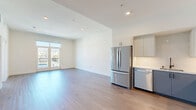 Located in the heart of Hollywood at 1233 N Highland, this modern 2-bedroom, 2-bathroom residence offers a thoughtfully designed open-concept layout with clean lines and contemporary finishes throughout. Light wood-style flooring runs continuously across the entire floor, complementing the crisp white walls and recessed lighting that keep the space bright and airy.

The combined kitchen and living area serves as the heart of the home, featuring stainless steel appliances including a French-door refrigerator and dishwasher, sleek gray cabinetry with black hardware, and a light countertop. French doors in the living area open to a private balcony, offering sweeping views of the Hollywood Hills and the surrounding cityscape.

Both bedrooms are well-proportioned and filled with natural light. The primary bedroom features French doors leading to the balcony, while the second bedroom benefits from large corner windows framing panoramic views. Each bedroom includes dedicated closet space. A barn-style door accent adds a modern-rustic touch to the hallway, which also provides access to in-unit laundry.

Both bathrooms are identically appointed with floor-to-ceiling large-format stone-look tile in the walk-in showers, mosaic tile shower floors, frameless glass sliding doors, and matte black fixtures, delivering a polished, spa-like aesthetic.