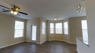 Located at 1211 Gray Birch Way in Knoxville, Tennessee, this two-story home offers a thoughtfully designed layout with functional living spaces spread across both floors. The main level is highlighted by a spacious living area featuring rich hardwood-style flooring, warm neutral-toned walls, and a striking bay window configuration that floods the room with natural light and adds an elegant architectural detail to the space. A glass-paneled exterior door provides additional light and outdoor access from this area. Track lighting on the ceiling offers flexible illumination, complementing the bright, airy atmosphere created by the multiple windows throughout. The floor plan reveals an open and connected layout on the main level, with a kitchen area equipped with cabinetry and appliances, and additional rooms that provide versatile living options. A staircase connects the two floors, leading to the upper level where additional living and sleeping spaces are situated. The upper floor continues the consistent design language seen below, maintaining the same neutral palette and hardwood-style flooring. Throughout the home, clean white trim and baseboards provide crisp contrast against the warm wall tones, contributing to a cohesive and well-finished interior aesthetic. The overall layout offers comfortable, functional living across both stories.