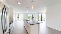 Located at 8001 S Sixth St in Oak Creek, WI, this thoughtfully designed single-floor residence offers three bedrooms and two bathrooms within a well-proportioned, open layout. The modern kitchen serves as a central hub, featuring a large island with a dark quartz countertop, undermount sink, white shaker cabinetry, a tile backsplash, stainless steel appliances, and elegant pendant lighting — all flowing seamlessly into the living area. Durable wood-look flooring runs throughout the main living spaces, while the bedrooms are finished with plush carpeting for added comfort. Large floor-to-ceiling windows in the living and bedroom areas invite abundant natural light and provide views of the surrounding landscape and neighborhood. The primary bedroom offers a generous footprint with a sliding-door closet and direct access to a private bathroom. The bathrooms are clean and contemporary, featuring white cabinetry with dark countertops, wood-look flooring, and a walk-in shower with a curved curtain rod. Additional bedrooms include closet storage and large windows. The overall aesthetic is clean, bright, and modern, with a neutral palette that creates a welcoming and versatile living environment throughout.