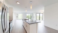 Located at 8001 S Sixth St in Oak Creek, WI, this thoughtfully designed single-floor residence offers three bedrooms and two bathrooms within a well-proportioned, open layout. The modern kitchen serves as a central hub, featuring a large island with a dark quartz countertop, undermount sink, white shaker cabinetry, a tile backsplash, stainless steel appliances, and elegant pendant lighting — all flowing seamlessly into the living area. Durable wood-look flooring runs throughout the main living spaces, while the bedrooms are finished with plush carpeting for added comfort. Large floor-to-ceiling windows in the living and bedroom areas invite abundant natural light and provide views of the surrounding landscape and neighborhood. The primary bedroom offers a generous footprint with a sliding-door closet and direct access to a private bathroom. The bathrooms are clean and contemporary, featuring white cabinetry with dark countertops, wood-look flooring, and a walk-in shower with a curved curtain rod. Additional bedrooms include closet storage and large windows. The overall aesthetic is clean, bright, and modern, with a neutral palette that creates a welcoming and versatile living environment throughout.