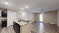 This single-floor residence offers a clean, modern design with a neutral color palette and wood-look flooring that flows seamlessly throughout every room. The open-concept layout connects the kitchen directly to the living area, creating a functional and social space ideal for everyday living. The kitchen is well-appointed with dark espresso cabinetry, granite countertops, a granite-topped island with an integrated sink, and a suite of appliances including a stainless steel refrigerator with ice and water dispenser, black electric range, built-in microwave, and dishwasher. Tall pantry cabinetry provides generous storage. The spacious living area is bright and airy, benefiting from natural light through a glass-panel exterior door and a ceiling fan with integrated lighting. The bedrooms continue the consistent flooring and neutral tones, each equipped with ceiling fans. The bathroom features a full tub-shower combination with chrome fixtures and matching flooring. A dedicated laundry area includes washer and dryer hookups, offering added convenience. Throughout the space, recessed lighting, clean white trim, and a cohesive warm-toned finish create a tidy, move-in-ready environment.