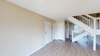 This two-floor home offers a clean, practical layout designed for comfortable everyday living. The main level entry area features light wood-style laminate flooring that extends throughout the space, providing a warm and cohesive aesthetic underfoot. Neutral beige walls create a welcoming atmosphere, complemented by crisp white trim and baseboards throughout.

The main level showcases a spacious open area with multiple doorways leading to additional rooms or storage spaces. A white-railed staircase is prominently positioned along one wall, providing a clean transition to the upper floor while also allowing natural light to filter in from nearby windows, brightening the entryway and main living area.

The textured popcorn ceiling adds a classic finish consistent throughout the main level. White interior doors with paneled detailing contribute to a tidy and uniform appearance across the space.

The overall design of this home is straightforward and functional, with an emphasis on clean lines and neutral tones that offer a versatile backdrop for a variety of interior styles. The two-floor configuration provides natural separation between living and private spaces, making the layout both practical and well-organized for daily use.