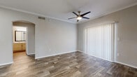 This efficiently designed 1-bedroom, 1-bathroom unit offers a functional and cohesive layout across a single floor. The entryway opens directly into a bright, open kitchen, which features light wood cabinetry, a white peninsula countertop with a built-in sink, and a full suite of stainless steel appliances including a refrigerator, electric range, and microwave. Wood-look tile flooring runs through the kitchen and living areas, providing a warm, durable foundation throughout the common spaces. The living room is accented with crown molding, a ceiling fan with integrated lighting, and a sliding glass door dressed with vertical blinds that allows for natural light and outdoor access. The bedroom is a comfortable size, finished with plush carpeting, crown molding, a ceiling fan, and a window with horizontal blinds. It connects to a generously sized walk-in closet outfitted with wire shelving and carpeted flooring. The bathroom is clean and functional, featuring wood-look tile flooring, a tub-shower combination with tiled surround, a light wood vanity, and a white countertop. Neutral tones and consistent finishes throughout contribute to a cohesive and move-in-ready ambiance.