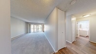 Located in Seattle, WA, this one-bedroom, one-bathroom unit offers a thoughtfully arranged single-floor layout that makes efficient use of its comfortable living space. The open-concept living and dining area is carpeted in soft, neutral tones and features a baseboard heating system, a textured ceiling, and a striking arched sliding glass door that opens to a private balcony with outdoor views — allowing natural light to fill the room. A ceiling fan adds to the practicality of the space.

The galley-style kitchen is well-appointed with white cabinetry, ample counter space, a double-basin sink, a dishwasher, and white electric range — all set above warm wood-look vinyl flooring that extends through the kitchen and into the bathroom and entry areas.

The generously sized bedroom features plush carpeting, a window with natural views, a built-in closet with sliding doors, and a baseboard heater. A separate closet provides additional storage.

The bathroom is clean and modern, highlighted by a soaking tub with a marble-patterned surround, chrome grab bars, a handheld showerhead, wood-look flooring, and a white vanity — combining both style and accessibility. The overall ambiance of the unit is neutral, bright, and move-in ready.