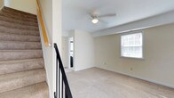 This two-story townhouse at Townhouse Farm offers a practical and comfortable layout spread across two levels. The kitchen is a standout feature, equipped with rich warm-toned wooden cabinetry that extends to the ceiling, providing generous storage throughout. Dark granite-style countertops contrast neatly with the cabinetry, while a full suite of black appliances — including a refrigerator, electric range, built-in microwave, and dishwasher — gives the space a cohesive, functional feel. A window above the sink allows natural light to brighten the area, and light tile flooring completes the kitchen's practical design.

The upper level features wall-to-wall carpeting that lends a comfortable, residential feel to the living spaces. A ceiling fan with an integrated light fixture provides both ventilation and ambient lighting. A window on the upper floor brings in natural light, enhancing the open, airy atmosphere of the room. A staircase with a wooden handrail and black metal balusters connects the two floors, adding a clean architectural detail to the home's interior. The neutral color palette throughout creates a versatile backdrop suitable for a variety of décor styles.