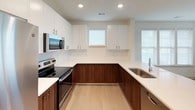 Located at The Basin, this single-floor residence offers a thoughtfully designed layout with a clean, contemporary aesthetic throughout. The open-concept living and dining area is anchored by light wood-style flooring, a ceiling fan, and an abundance of natural light streaming through multiple large windows fitted with blinds. A sliding door provides access to the outdoors, further enhancing the airy feel of the main living space.

The kitchen is a standout feature, boasting a two-tone design with white upper cabinetry and rich walnut-toned lower cabinets, complemented by white quartz countertops and a subway tile backsplash. Stainless steel appliances — including a refrigerator, range, microwave, and dishwasher — complete this functional and stylish space. A peninsula with seating potential connects the kitchen seamlessly to the living area.

The bedrooms are finished with plush carpeting and ceiling fans, each featuring windows that invite natural light and outdoor views. A walk-in closet with wire shelving provides generous storage in the primary suite. The primary bathroom offers a lengthy dual-sink vanity with modern hardware and tile flooring, while a secondary bathroom features a full tub-shower combination and neutral tile finishes throughout.