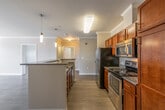 This single-floor residence is designed with a practical and cohesive aesthetic throughout. The kitchen serves as a central highlight, featuring rich, warm-toned wood cabinetry paired with dark granite countertops and a peninsula island ideal for casual dining or meal preparation. Stainless steel appliances, including a refrigerator, range, and over-the-range microwave, complement the space, while pendant lighting adds a polished finishing touch. Crown molding runs throughout the main living areas, lending an elevated architectural detail to the otherwise clean, neutral walls.

The living areas are finished with wood-style hard surface flooring in a light-to-medium tone, creating a consistent and easy-to-maintain foundation across the unit. The open layout connects the kitchen to the main living space, allowing for a fluid flow between areas.

The bedrooms are well-proportioned and bright, each benefiting from windows that invite natural light and provide views of surrounding greenery. The bathrooms are finished with tile flooring, wood-toned vanities, light countertops, large mirrors, and chrome fixtures. Grab bars are present in at least one bathroom, adding a functional accessibility feature. Overall, the space presents a clean, move-in-ready environment with consistent finishes throughout.