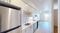 Located at 7007 SW Hampton St in Tigard, Oregon, this thoughtfully designed single-floor unit offers a clean, modern aesthetic with an efficient layout. The galley-style kitchen is a standout feature, outfitted with white flat-panel cabinetry extending to the ceiling, white quartz countertops, a subway tile backsplash, stainless steel appliances including a Frigidaire refrigerator, a built-in dishwasher, and a sleek range with an overhead hood. Light wood-tone flooring runs continuously throughout, tying the spaces together cohesively. The hallway connects the kitchen to the open living area, which benefits from a large window that draws in abundant natural light and provides views of the surrounding landscape. The living room also features recessed lighting and a wall-mounted mini-split HVAC unit, ensuring year-round comfort. A built-in shelf adds a subtle architectural detail to the space. The bathroom is designed with accessibility in mind, featuring grab bars and wood-tone flooring that complements the rest of the unit. Crisp white walls and recessed lighting throughout give the entire space a bright, contemporary feel, making it a well-appointed and functional unit in the heart of Tigard.