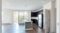 Located at 6010 Attleboro Dr in Cary, NC, this single-floor residence offers four bedrooms, two bathrooms, and a thoughtfully designed open layout. The kitchen and living area form a seamless, light-filled hub at the heart of the home. The kitchen is appointed with dark espresso cabinetry, stainless steel appliances including a refrigerator, range, and microwave, and a curved granite-topped island with a built-in sink and pendant lighting overhead. Large windows and a balcony access door flood the space with natural light and offer views of surrounding greenery. Wood-look flooring runs throughout the main living and bedroom areas, lending a warm, cohesive aesthetic. The primary bedroom is generously sized and served by a well-appointed bathroom featuring a dual-sink dark vanity, wood-look tile flooring, and a glass-enclosed walk-in shower. Additional bedrooms are carpeted and each receive natural light through window treatments. A dedicated laundry room houses a full-size front-loading washer and dryer with built-in overhead shelving. Two closets, including a walk-in with wire shelving systems, provide ample storage. Two hallways connect the rooms efficiently, and the clean, neutral palette throughout creates a bright, move-in-ready atmosphere.