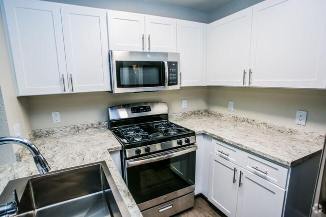 Stainless steel microwave and gas range with white shaker cabinets, granite counter, and large sink. - The Lido Apartments