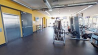 This fitness center is a comprehensively outfitted space designed to accommodate a full range of workout needs. The open floor plan is finished with durable dark rubber flooring throughout, providing a clean, functional foundation for all types of exercise.

The cardio zone features a lineup of treadmills, elliptical trainers, and stationary bikes positioned along a wall of large floor-to-ceiling windows. These windows flood the space with natural light and offer views of the surrounding outdoor environment, creating an energizing atmosphere during workouts. Multiple wall-mounted flat-screen TVs are positioned throughout the space for entertainment.

The strength training area is well-stocked with a diverse selection of equipment, including a multi-functional cable machine, a leg press, a full rack of kettlebells, dumbbells in varying weights, barbells with weight plates, and additional resistance machines. A large wall mirror aids in form correction during training sessions.

Exposed industrial-style ductwork runs along the ceiling, contributing to the space's modern aesthetic. Accent walls painted in a bold yellow add energy and visual contrast to the otherwise neutral interior. The fitness center also includes a dedicated restroom, a water fountain, and ample open floor space for stretching or functional training exercises.