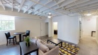 This single-floor unit showcases a distinctive industrial aesthetic defined by its soaring exposed beam ceilings, painted white to create a clean, contemporary contrast against the open layout below. Polished concrete floors extend throughout the main living areas, contributing to the loft-inspired character of the space.

The open-concept living and dining area is generously proportioned, offering ample room for both lounging and casual dining. A ceiling fan provides comfort, while pendant lighting complements the industrial framework overhead. A window in the dining area invites natural light, enhancing the bright, airy atmosphere of the space.

The kitchen runs along one wall and is well-equipped with stainless steel appliances, including a refrigerator, electric range, built-in microwave, and dishwasher. Dark espresso cabinetry extends from floor to ceiling, paired with granite-style countertops that add a refined touch to the utilitarian design aesthetic.

The bathroom is compact and functional, featuring a dark vanity with a granite countertop, a wall-mounted mirror, and polished concrete flooring consistent with the rest of the unit. The crisp white walls and flush ceiling light keep the space feeling clean and uncluttered.

Overall, the unit balances raw, industrial elements with modern finishes to create a cohesive and stylish living environment.