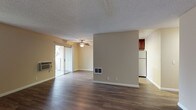 This single-floor residence offers a practical and well-appointed layout across several distinct living spaces. The open living and dining area is a standout, featuring dark hardwood-style flooring, warm beige walls, and a textured ceiling. A ceiling fan with a light fixture anchors the room, while a wall-mounted air conditioning unit provides climate control. Sliding glass doors lead to an outdoor area, allowing natural light to fill the space. A floor vent and additional window further enhance airflow and brightness.

The galley-style kitchen is efficiently designed with rich dark wood cabinetry lining both sides, granite-look countertops, a double stainless steel sink, and stainless steel appliances including a refrigerator, electric range, and over-the-range microwave. Light wood flooring and overhead lighting complete the functional workspace.

The bedrooms are carpeted for comfort, featuring neutral tones, baseboard heating, sliding closet doors, and windows that offer views of surrounding greenery. The bathroom includes a dark wood vanity with granite countertops, a large mirror with overhead lighting, a tiled tub-shower combination, and an adjacent walk-in closet area, offering a practical and organized layout.