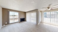 This single-story 2-bedroom, 3-bathroom residence is thoughtfully laid out across a comfortable footprint, offering a practical and cohesive living environment. The living room serves as the heart of the home, featuring plush wall-to-wall carpeting, a textured ceiling, and a wood-burning fireplace set on a brick hearth. Multiple windows and a sliding glass door dressed with vertical blinds fill the space with natural light and provide direct outdoor access and exterior views. A second sliding glass door is found in one of the bedrooms, further connecting the interior to the outside. Both bedrooms are carpeted and equipped with ceiling fans with light fixtures, offering a comfortable and functional retreat. The primary bedroom includes a spacious sliding-door closet, while the secondary bedroom also features closet storage. Three bathrooms serve the residence, including one with a tub-shower combination accented by white tile surround, and another featuring a standalone shower unit with wood-look flooring. Granite-style countertops are noted in the bathroom vanity areas. A kitchen, hallways, and additional closets round out the floor plan, providing ample storage and circulation throughout. The overall aesthetic is neutral and move-in ready, with warm beige tones throughout.