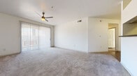 This single-floor residence offers a clean, neutral aesthetic throughout, with a thoughtful layout designed for comfortable everyday living. The spacious living area is finished with plush wall-to-wall carpeting and features a ceiling fan with light, a sliding glass door fitted with vertical blinds that allows natural light to fill the room and provides access to an outdoor space. HVAC vents are integrated into the ceiling for year-round climate control. The kitchen is efficiently designed with white cabinetry, dark countertops, and a full suite of black appliances including an electric range, over-the-range microwave, and refrigerator, all set over easy-care wood-look vinyl flooring. The bedrooms continue the carpeted theme, each offering ceiling fans, ample natural light through vertical-blind-covered windows, and generous floor space. The bathrooms are finished with wood-look vinyl flooring, white cabinetry with dark countertops, large mirrors, and bright vanity lighting. One bathroom includes a full tub-shower combination, while another features a private water closet and a separate mirrored closet area, adding functionality and privacy. The overall palette of white walls and neutral tones creates a bright, clean environment throughout the space.