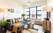 Located at 728 Bergen Avenue in Jersey City, NJ, this modern single-floor residence offers a thoughtfully designed open-concept layout with clean lines and contemporary finishes throughout. The kitchen is a standout feature, equipped with stainless steel appliances including a gas range, microwave, and full-size refrigerator, complemented by wood-toned cabinetry and a quartz-topped peninsula with seating for two — ideal for casual dining or entertaining. Light wood flooring flows seamlessly into the living area, which is bathed in natural light from large, bold-framed windows offering open urban views of the Jersey City streetscape. The living space provides a welcoming atmosphere with ample room for comfortable seating and a dedicated workspace. The bedroom continues the bright, airy aesthetic, featuring oversized windows that frame outdoor views and fill the room with daylight. The bathroom is finished with a dark wood vanity topped with white quartz, a large mirror, and a glass-enclosed walk-in shower with tile surround, creating a clean and spa-like feel. Throughout the residence, recessed lighting, neutral wall tones, and light flooring combine to create a cohesive, modern ambiance well-suited to contemporary urban living.