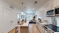 This single-floor residence showcases a thoughtfully designed open-concept layout that seamlessly connects the kitchen, dining, and living areas. The kitchen is outfitted with light wood grain cabinetry extending to the ceiling, white quartz countertops, a full suite of stainless steel appliances, and a generous island with bar seating illuminated by pendant lighting overhead. White subway tile backsplash adds a clean, contemporary touch.

The living area benefits from natural light streaming through large windows and features durable light wood-toned flooring that runs throughout the main living spaces. The space offers a comfortable, airy feel with neutral walls and recessed lighting.

The primary bedroom is a well-proportioned retreat with carpet flooring, a large window, and double closet doors providing ample storage. Its en-suite bathroom features light wood vanity cabinetry, dual sinks, white quartz countertops, a large mirror, and a tiled walk-in shower. The second bedroom is equally inviting with natural light and its own access to a full bathroom featuring gray subway tile surrounding a soaking tub-shower combination and matching wood-toned cabinetry. Throughout, the design maintains a cohesive modern aesthetic with clean lines and a warm, neutral palette.