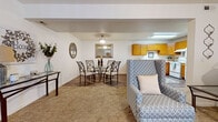 This single-floor residence is thoughtfully designed with an open-concept layout that seamlessly connects the living, dining, and kitchen areas into one cohesive, functional space. The living room features plush carpeting, a sliding glass door that allows natural light to filter in, and ample room for comfortable seating arrangements. A decorative mirror accents the neutral-toned walls, enhancing the sense of openness throughout.

The dining area transitions naturally from the living space, featuring wood-look flooring and room for a full dining set. It flows directly into the kitchen, which is equipped with warm honey-toned wood cabinetry offering generous storage, white appliances including a refrigerator, range, and dishwasher, and light countertops. The U-shaped kitchen layout maximizes workspace and efficiency.

A dedicated laundry room provides added convenience, housing a water heater and connections for a washer and dryer, with additional storage shelving overhead. The bedroom area offers a quiet retreat with a window providing natural light. Throughout the residence, the combination of carpet and wood-look flooring, neutral walls, and practical finishes creates a clean, welcoming ambiance well-suited for everyday living.