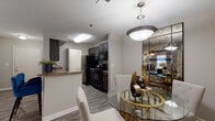 This single-floor residence offers a thoughtfully designed layout that balances comfort and functionality across its key living spaces. The open-concept living and dining area serves as the heart of the home, finished with wood-style plank flooring, neutral-toned walls, and a textured ceiling with a ceiling fan overhead. A sliding glass door floods the living room with natural light and opens to a private balcony with tree-lined views, creating a seamless indoor-outdoor connection. The dining area features an elegant glass-top table with pendant lighting, anchored beside a mirrored accent wall.

The galley-style kitchen is well-equipped with dark cabinetry, granite-style countertops, and a full suite of black appliances including a refrigerator, range, microwave, and dishwasher. A pass-through counter connects the kitchen to the dining space, enhancing the open flow of the unit.

The bedroom is a serene retreat, carpeted for warmth and comfort, with a ceiling fan, soft neutral tones, and generous wall space for artwork. The full bathroom includes dark wood vanity cabinetry with granite-style countertops, wood-look tile flooring, a soaking tub, and a separate glass-enclosed shower. A dedicated laundry area with wire shelving completes this well-rounded residence.