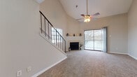 This two-story residence is defined by its striking vaulted ceilings in the main living area, which create an expansive, airy atmosphere complemented by a ceiling fan with integrated lighting. A staircase with sleek black metal railings leads to the upper level, adding a contemporary architectural detail. The living room centers around a fireplace with a clean white mantel and offers direct access to an outdoor balcony through a large sliding glass door, allowing generous natural light to flow in.

The kitchen is well-appointed with gray cabinetry, white countertops, light wood-style flooring, and a full suite of black appliances including a range, microwave, refrigerator, and dishwasher. A peninsula counter separates the kitchen from the adjacent carpeted living area. A dedicated in-unit laundry space with shelving is conveniently located nearby.

The bedrooms are generously sized with high ceilings, plush carpeting, and ceiling fans. One bedroom features a door with exterior access and a double sliding-door closet, while another connects directly to a bathroom. The bathrooms include a soaking tub with tiled surround and a separate full bath with a shower-tub combination, vanity, and wood-style flooring throughout.