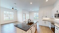 Located in Huntersville, NC, this well-appointed single-floor residence offers a thoughtfully designed open-concept layout that maximizes comfort and functionality. Warm hardwood-style flooring flows throughout every room, complemented by crisp white walls that create a bright, clean aesthetic.

The combined kitchen and living area serves as the heart of the home. The kitchen is outfitted with white shaker-style cabinetry featuring matte black hardware, dark granite countertops, a subway tile backsplash, and stainless steel appliances. A built-in desk nook with under-cabinet lighting and a wine rack add practical, stylish touches. The living area benefits from large windows that flood the space with natural light and a ceiling fan overhead.

The spacious bedroom continues the light-filled theme, with multiple windows offering outdoor views of the surrounding greenery. A dedicated walk-in closet features built-in shelving and hanging rods, providing generous storage.

The bathroom is finished in a consistent modern style, with white cabinetry, dark granite countertops, matte black fixtures, a tiled tub-shower combination, and a framed mirror. A hallway connects the spaces cohesively, completing this clean, contemporary residence.