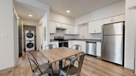 Located at 400 Schweitzer Plaza Drive in Ponderay, Idaho, this single-floor unit offers a clean, modern design throughout. The open-concept kitchen is well-appointed with white shaker-style cabinetry, dark countertops, stainless steel appliances including a range, dishwasher, and refrigerator, and wood-look luxury vinyl plank flooring that extends throughout the entire space. A dining area adjacent to the kitchen provides convenient everyday functionality, while a stacked washer and dryer unit is conveniently situated nearby.

The living room is bright and inviting, featuring a wall-mounted television and large sliding glass doors that open onto a private balcony, allowing natural light to fill the space and providing outdoor views of the surrounding area. A wide entryway hallway connects the main living areas to the private quarters.

The primary bedroom features a sliding closet door for efficient storage, while the second bedroom includes a window with views of the surrounding landscape, making it a comfortable and versatile space. The full bathroom is finished with white shaker cabinetry, a dark countertop vanity, a mirror, and a bathtub/shower combination. Clean lines, neutral tones, and consistent flooring throughout give this unit a cohesive and contemporary feel.