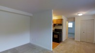 This single-floor unit is organized into a practical, efficient layout that maximizes its available footprint. The floor plan reveals two main living areas positioned on either side of a central kitchen, creating a clear sense of separation between the living and sleeping spaces.

The living area features neutral carpet flooring and clean white walls, providing a blank canvas for personalization. The space is open and simply designed, with standard ceiling height and understated trim work along the baseboards.

The kitchen occupies a central position within the unit and is equipped with a black gas range and oven, complemented by warm wood-toned upper cabinetry. The kitchen features hardwood flooring, which contrasts with the carpeted areas throughout the rest of the unit. A range hood is installed above the stove, and the compact layout keeps all essentials within easy reach.

The bedroom, located on the opposite side of the kitchen, offers carpeted flooring consistent with the living area and includes a set of double-door closets, providing ample storage. A window in the bedroom allows natural light to filter into the space. Overall, the unit presents a clean, functional design well-suited for everyday living.