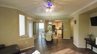 This single-story residence offers a thoughtfully designed open-concept floor plan that promotes a natural flow between living spaces. Rich, dark hardwood flooring extends throughout the main living areas, grounding the space with warmth and elegance. Crown molding frames the ceilings, adding a refined architectural detail that enhances the overall character of the home.

The dining area serves as a central gathering point, anchored by a round dining table with cream upholstered chairs and topped by a stylish ceiling fan with integrated lighting. Natural light filters in through multiple windows, including a bright entry area that adds an airy, welcoming quality to the space.

Transitioning seamlessly from the dining area, the kitchen is well-equipped with white cabinetry, black appliances including a refrigerator and microwave, and a kitchen island that offers additional prep and storage space. Pendant lighting above the island adds a functional yet decorative touch.

Warm, neutral-toned walls tie the interior together, complementing both the flooring and cabinetry throughout. The layout is practical and open, making the space feel connected and easy to navigate. Overall, this home combines classic design elements with everyday functionality, creating a comfortable and inviting living environment.