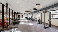 Located at 110 Field St in Newnan, GA, this single-floor fitness center offers a generously sized, open-plan workout space designed to accommodate a wide range of exercise disciplines. The facility features an industrial-inspired aesthetic, with exposed ductwork running along the ceiling, ceiling fans, and sleek linear pendant lighting that collectively create a modern, loft-like atmosphere.

The main workout floor is carpeted and bathed in natural light from a series of multi-pane windows lining the walls. A dedicated cardio zone houses multiple treadmills and stationary bikes equipped with personal display screens, ideal for guided or self-directed training sessions. Alongside the cardio equipment, a cable machine and power rack provide strength training options, while a sled trainer and large tire support functional and high-intensity workouts.

A separate area is defined by full-height black-framed glass partition walls, creating a distinct studio or lounge space visible from the main floor. This zone adds versatility to the facility, suitable for stretching, group classes, or recovery. A well-stocked equipment rack along one wall holds kettlebells, medicine balls, resistance bands, and other accessories, ensuring a comprehensive training experience. The overall design balances functionality and aesthetic appeal, making this a practical and inviting fitness destination.