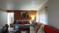 This single-floor home offers a thoughtfully arranged layout that balances comfort and functionality across its main living spaces. The living room serves as the heart of the home, featuring rich hardwood-style flooring, a textured ceiling, and a bold terracotta accent wall that adds warmth and character. Large windows dressed with sheer curtains allow natural light to fill the room, complementing the cozy seating arrangement centered around a wooden coffee table.

The kitchen is efficiently designed with dark espresso cabinetry, granite-style countertops, a tile mosaic backsplash, and black appliances including a full-size refrigerator and range. A peninsula counter provides additional prep space and a subtle division between the kitchen and adjacent dining area.

The bedroom is a cheerful, well-lit space with neutral gray walls, hardwood-style flooring, and a window that invites natural light and outdoor views. The room also features a closet, offering practical storage.

The bathroom is neatly finished with a dark wood vanity, granite-style countertop, a tub-shower combination with a decorative curtain, and coordinating hardwood-style flooring that ties together the home's consistent aesthetic. Overall, the space presents a warm and livable environment with cohesive design choices throughout.