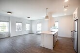 Located at 52 E Main St in Bay Shore, NY, this single-floor unit showcases a clean, contemporary design with a cohesive palette of whites and warm neutral tones throughout. Light wood-style flooring runs continuously across the living areas, bedrooms, and hallways, lending a sense of openness and flow to the entire space.

The open-concept living and kitchen area is a standout feature, with multiple windows allowing generous natural light and views of the surrounding streetscape. The kitchen is outfitted with white shaker-style cabinetry, white quartz countertops, a subway tile backsplash, and stainless steel appliances including a range and over-the-range microwave. A peninsula with a pendant light above provides additional workspace and separates the kitchen from the living area.

Bedrooms are well-proportioned, each benefiting from large windows and wall-unit HVAC systems. At least one bedroom includes access to a dedicated walk-in closet. Connecting the rooms is a bright, clean hallway with recessed lighting and multiple panel doors with brushed nickel hardware.

The bathroom features marble-look porcelain tile flooring, a white vanity with a gray stone-style countertop, a framed mirror, and a glass-enclosed walk-in shower with white subway tile surround and chrome fixtures.