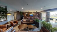 Located at 28294 Ferry Rd in Warrenville, Illinois, this thoughtfully designed amenity floor offers a rich collection of social, recreational, and wellness spaces all on a single level. The central lounge sets an immediate tone of sophistication, featuring rich leather seating, warm wooden accents, a textured feature wall, an artistic round mirror, and cascading Edison bulb pendant lighting that creates an inviting, upscale ambiance. Lush indoor plants and a mounted TV complete the comfortable gathering space. Adjacent dining and lounge areas offer a variety of seating arrangements, from cozy booth-style banquettes on warm hardwood flooring to a soft blue-accented room adorned with sculptural wall art and plush lounge chairs. A sleek, modern fireplace lounge with stone cladding, a linear gas fireplace, a circular LED chandelier, and dark wood slatted walls provides an intimate retreat. The chef's kitchen stands out with dramatic black marble countertops, custom wood cabinetry, geometric pendant lighting, and full appliances, ideal for entertaining. The expansive fitness center is equipped with ellipticals, treadmills, a rowing machine, strength training equipment, and a dedicated turf training zone, all bathed in natural light with outdoor views.