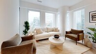 Located in the heart of Toronto's Financial District at Adelaide St W, this thoughtfully designed three-bedroom, two-bathroom residence offers a refined urban living experience. The open-concept layout connects the living room and kitchen seamlessly, with the living area anchored by expansive floor-to-ceiling windows that frame striking city skyline views and flood the space with natural light. Distinctive herringbone light wood flooring runs throughout, adding warmth and visual continuity.

The kitchen features sleek flat-panel cabinetry in warm tones, integrated appliances, and a clean white countertop, blending functionality with modern aesthetics. The entry hallway sets an elegant tone with curated wall art and a peek into the bright, airy living spaces beyond.

Each bedroom is bright and comfortable, with the primary bedroom benefiting from large windows overlooking the Toronto skyline, creating a calm and light-filled retreat. The secondary bedrooms are equally well-appointed with natural light and clean, neutral finishes.

Both bathrooms are finished with sage-green vertical subway tiles, deep soaking tubs, glass enclosures, and dark bronze fixtures — a refined spa-like aesthetic. Throughout the residence, matte black and dark bronze hardware details provide a cohesive, contemporary touch.