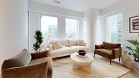 Located in the heart of Toronto's Financial District at Adelaide St W, this thoughtfully designed three-bedroom, two-bathroom residence offers a refined urban living experience. The open-concept layout connects the living room and kitchen seamlessly, with the living area anchored by expansive floor-to-ceiling windows that frame striking city skyline views and flood the space with natural light. Distinctive herringbone light wood flooring runs throughout, adding warmth and visual continuity.

The kitchen features sleek flat-panel cabinetry in warm tones, integrated appliances, and a clean white countertop, blending functionality with modern aesthetics. The entry hallway sets an elegant tone with curated wall art and a peek into the bright, airy living spaces beyond.

Each bedroom is bright and comfortable, with the primary bedroom benefiting from large windows overlooking the Toronto skyline, creating a calm and light-filled retreat. The secondary bedrooms are equally well-appointed with natural light and clean, neutral finishes.

Both bathrooms are finished with sage-green vertical subway tiles, deep soaking tubs, glass enclosures, and dark bronze fixtures — a refined spa-like aesthetic. Throughout the residence, matte black and dark bronze hardware details provide a cohesive, contemporary touch.