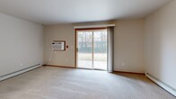 Located at 540 McKinley Ave in Clintonville, Wisconsin, this single-floor, 2-bedroom, 1-bathroom unit offers a practical and comfortable layout throughout. The combined kitchen and living area forms the heart of the home, with the kitchen featuring warm oak cabinetry, black appliances including a refrigerator, dishwasher, and electric range with built-in microwave, and wood-look luxury vinyl flooring. The living room is generously sized and bathed in natural light, with plush carpet underfoot and a large sliding glass door that opens to an outdoor patio area with views of surrounding greenery. A wall-mounted AC unit provides additional climate control alongside baseboard heating found throughout the unit. Both bedrooms are well-proportioned, carpeted, and equipped with ceiling fans and natural light from windows. The primary bedroom features a walk-in closet with built-in shelving and hanging rods, offering ample storage. A second closet provides additional organization space. The full bathroom showcases wood-look tile flooring, oak vanity cabinetry, a soaking tub with grab bar, and a clean, neutral finish. Warm wood trim accents and a consistent neutral color palette tie the space together, creating a cohesive and move-in-ready living environment.