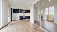 Located at 140 Ferguson Dr in Woodstock, Ontario, this thoughtfully designed one-bedroom unit offers a bright and contemporary living experience across a single floor. Light-toned hardwood flooring flows seamlessly throughout the entire space, complementing the clean white walls and creating a warm, cohesive aesthetic.

The open-concept living area is bathed in natural light, courtesy of a large sliding glass door flanked by floor-to-ceiling windows that frame outdoor views of the surrounding greenery and streetscape. This wall of glazing provides excellent ventilation and a strong connection to the outdoors.

The kitchen is compact yet well-appointed, featuring bold dark cabinetry that contrasts beautifully with a classic white subway tile backsplash. Stainless steel appliances, including an electric range and built-in microwave, lend a modern edge, while open shelving and a built-in desk area add functional versatility to the space.

The bedroom is accessed through sleek mirrored sliding doors that visually expand the room while reflecting natural light from the main living area. The bedroom itself is a calm, minimalist retreat with clean lines and ample wall space.

The overall ambiance of the unit is modern and airy, with a neutral palette and quality finishes that provide a refined yet functional living environment.