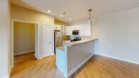 Located at 17444 Slipper Shell Way in Lewes, Delaware, this well-appointed 2-bedroom, 2-bathroom residence offers a thoughtfully designed single-floor layout that maximizes comfort and functionality. Light wood-style flooring flows throughout the main living areas, lending a clean, modern aesthetic from the moment you enter through the welcoming hallway.

The open-concept kitchen and living room serve as the heart of the home. The kitchen is equipped with stainless steel appliances — including a refrigerator, gas range, microwave, and dishwasher — complemented by white cabinetry with glass-front upper cabinets, neutral countertops, a peninsula with bar seating, and stylish pendant and track lighting. The adjacent living area is bright and airy, highlighted by a sliding glass door that opens onto a private balcony, inviting natural light and outdoor views into the space.

Both bedrooms are carpeted and feature ceiling fans, generous windows with blinds, and ample natural light. The spacious primary bedroom offers a comfortable retreat with a well-sized walk-in closet fitted with wire shelving. The two bathrooms are finished with large-format white tile flooring, white vanities, and natural light from windows. Additional storage is provided by two closets throughout the home, rounding out a practical and inviting living space.