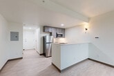 Located at 3190 S Vaughn Way in Aurora, Colorado, this efficiently designed single-floor unit offers a thoughtfully arranged layout that maximizes every square foot of its compact footprint. Light wood-style flooring runs continuously throughout the space, lending a clean and cohesive aesthetic.

The kitchen is a standout feature, equipped with stainless steel appliances including a full-size refrigerator, microwave, and range. Gray cabinetry provides ample storage, while a white peninsula counter offers additional workspace and serves as a natural divider between the kitchen and the open living area. Recessed lighting and a wall sconce keep the kitchen well-lit and functional.

The open living area benefits from a large window that invites natural light and provides views of the surrounding neighborhood. Vaulted ceiling lines add a sense of vertical openness to the space. A wall-mounted HVAC unit ensures year-round climate control.

The bathroom is clean and practical, featuring a wide white vanity with an integrated sink, a large mirror with overhead lighting, towel bars, and matching light wood-style flooring that ties into the rest of the unit.

A welcoming entryway corridor connects all areas of the unit, offering a logical and organized flow throughout. The overall ambiance is bright, modern, and move-in ready.