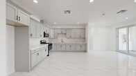 Located at 16220 Arrow Blvd in Fontana, CA, this well-appointed 3-bedroom, 2-bathroom single-story home offers a clean, modern aesthetic carried consistently throughout every room. Gleaming large-format marble-look porcelain tile floors flow seamlessly across the entire living space, creating a bright and cohesive atmosphere.

The open-concept kitchen and living area serves as the heart of the home. The kitchen is outfitted with soft gray shaker-style cabinetry, striking marble-look backsplash, white quartz countertops, and stainless steel appliances including a gas range and built-in microwave — all complemented by recessed lighting above.

Both bathrooms echo the home's refined palette, featuring matching marble-look tile floors, white quartz vanity tops, shaker-style cabinetry, matte black fixtures, and sleek sliding glass-enclosed shower enclosures with dark framing accents. An illuminated vanity mirror adds a modern touch.

Each of the three bedrooms is bright and airy, benefiting from natural light admitted through windows fitted with horizontal blinds and offering neighborhood views. Ceiling fans provide comfort in every bedroom. The primary bedroom offers a generously sized layout with ample closet space.

A dedicated laundry room with side-by-side washer and dryer hookups rounds out this thoughtfully designed home.