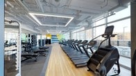 This contemporary fitness center offers a thoughtfully designed, single-floor layout that maximizes both functionality and comfort. The space is defined by an expansive wall of floor-to-ceiling windows along one side, flooding the interior with abundant natural light and providing views of the surrounding urban streetscape. The bright, airy atmosphere is further enhanced by a white exposed ceiling fitted with recessed rectangular LED lighting panels, giving the space a clean, industrial-modern aesthetic.

The main floor features a long central stretch of hardwood flooring, lined with a row of treadmills and cardio machines, including stair climbers, creating an organized and accessible workout corridor. To the left, rubberized flooring hosts a dedicated free weights and strength training area, complete with adjustable benches and additional equipment. A bold graphic mural in yellow, blue, and white anchors the far end of the space, adding a dynamic visual focal point. Mirrored walls in the strength zone enhance the sense of openness while supporting proper form during exercise. The overall layout is spacious, uncluttered, and well-organized for a well-rounded fitness experience.