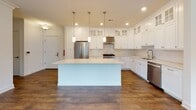 Located at 25 Mill St in Bernardsville, NJ, this single-floor residence combines modern finishes with a thoughtfully designed layout. The open-concept living area is anchored by rich hardwood-style flooring, crown molding, recessed lighting, and natural light streaming through multiple windows and a glass-paned exterior door.

The gourmet kitchen is a standout feature, showcasing floor-to-ceiling white shaker cabinetry with glass-front upper cabinets, light stone countertops, a subway tile backsplash, and stainless steel appliances including a gas range with a stainless hood. A generous center island with pendant lighting above provides ample workspace and serves as a natural gathering point.

The primary bathroom is elegantly appointed with dual white vanities, brushed gold hardware, light stone countertops, large mirrors, and a glass-enclosed walk-in shower accented with a decorative tile inlay. A secondary full bathroom offers a soaking tub and shower combination with textured tile surround, a white vanity, and polished nickel fixtures. Two spacious walk-in closets feature wire shelving systems and hardwood-style flooring, offering generous storage capacity. A dedicated laundry room houses a full-size washer and dryer with upper white cabinetry for additional storage. The overall aesthetic is clean, contemporary, and move-in ready.