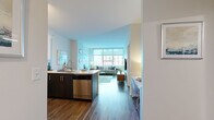 This well-appointed 1-bedroom, 1-bathroom unit is thoughtfully designed with a modern aesthetic and functional open-concept layout. Rich hardwood-style flooring flows throughout, tying each space together seamlessly.

The kitchen is a standout feature, outfitted with sleek two-tone cabinetry — crisp white uppers paired with dark lower cabinets — and a suite of stainless steel appliances including a refrigerator, range, microwave, and dishwasher. A white quartz peninsula with an undermount sink offers additional prep space and casual seating.

The living room is bathed in natural light through expansive floor-to-ceiling windows framing sweeping urban views, creating a bright and airy atmosphere. A private balcony extends the living space outdoors.

The bedroom is a calm retreat, featuring hardwood-style flooring, a large window with roller shades, and a dedicated closet with built-in shelving. The full bathroom is finished with marble-style tile flooring, a dark vanity with a white countertop, a large mirror, and a shower-tub combination.

Additional conveniences include an in-unit laundry room with a full-size washer and dryer, plus an overhead shelf for storage. A dedicated closet completes this efficiently organized home.