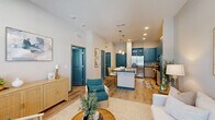 This well-designed one-bedroom, one-bathroom residence in Titusville, Florida offers a thoughtfully laid-out single-floor plan with a cohesive modern aesthetic. Wood-look plank flooring runs throughout the space, lending warmth and continuity to every room.

The open-concept kitchen is a standout feature, showcasing bold teal upper cabinetry paired with light wood lower cabinets and dark granite countertops. A large center island with a farmhouse sink and pendant lighting serves as both a prep area and casual dining space. Stainless steel appliances, including a French door refrigerator, range, and built-in microwave, complete the fully equipped kitchen. A geometric patterned tile backsplash adds a decorative touch.

The living room is bright and airy, benefiting from an abundance of natural light through large windows with views of the surrounding greenery. Elevated ceilings amplify the sense of openness in the space.

The bedroom is a calm, neutral retreat featuring dual windows that bring in soft natural light. A dedicated closet provides practical storage.

The bathroom is finished with large-format grey tile surrounding the soaking tub and shower combination, complemented by a granite-topped vanity and warm wood cabinetry. Teal-painted doors throughout the residence provide a consistent and distinctive design accent that ties the entire space together.