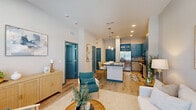 This well-designed one-bedroom, one-bathroom residence in Titusville, Florida offers a thoughtfully laid-out single-floor plan with a cohesive modern aesthetic. Wood-look plank flooring runs throughout the space, lending warmth and continuity to every room.

The open-concept kitchen is a standout feature, showcasing bold teal upper cabinetry paired with light wood lower cabinets and dark granite countertops. A large center island with a farmhouse sink and pendant lighting serves as both a prep area and casual dining space. Stainless steel appliances, including a French door refrigerator, range, and built-in microwave, complete the fully equipped kitchen. A geometric patterned tile backsplash adds a decorative touch.

The living room is bright and airy, benefiting from an abundance of natural light through large windows with views of the surrounding greenery. Elevated ceilings amplify the sense of openness in the space.

The bedroom is a calm, neutral retreat featuring dual windows that bring in soft natural light. A dedicated closet provides practical storage.

The bathroom is finished with large-format grey tile surrounding the soaking tub and shower combination, complemented by a granite-topped vanity and warm wood cabinetry. Teal-painted doors throughout the residence provide a consistent and distinctive design accent that ties the entire space together.