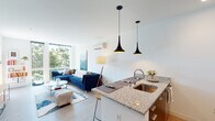 This single-floor residence showcases a contemporary open-concept design that seamlessly integrates the kitchen, dining, and living areas into one cohesive space. Light hardwood flooring runs throughout, complementing the clean white walls and lending warmth to the modern aesthetic.

The kitchen features granite countertops extending across a peninsula with seating, dark wood cabinetry contrasted by white upper cabinets, and a full suite of stainless steel appliances including a refrigerator, range, and microwave. Striking black pendant lights hang above the peninsula, adding a design focal point.

The living area benefits from floor-to-ceiling windows that frame lush greenery views, flooding the space with natural light. A wall-mounted mini-split system provides climate control. The open layout allows for generous furniture arrangement, and the connection to the kitchen creates an ideal environment for entertaining.

Both bedrooms are well-proportioned, each featuring windows with outdoor views and ample natural light. A wall-mounted mini-split unit in the primary bedroom ensures year-round comfort.

The bathroom is cleanly finished with granite countertops, white cabinetry, a large mirror, and a tub-shower combination. Light hardwood-style flooring ties the bathroom's design to the rest of the unit, creating a cohesive, polished finish throughout.