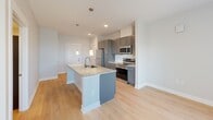 This efficiently designed one-bedroom, one-bathroom residence in Indianapolis, IN offers a well-organized single-level layout with contemporary finishes throughout. The open-concept kitchen serves as the centerpiece of the living area, featuring a granite-topped island with an undermount sink, pendant lighting, gray shaker-style cabinetry, a subway tile backsplash, and a full suite of stainless steel appliances including a refrigerator, electric range, and built-in microwave. Light wood-tone flooring runs throughout the main living area, enhancing the bright, airy feel created by recessed and pendant lighting.

The bedroom offers plush carpeting, a ceiling fan, and two windows that provide natural light and views of the Indianapolis skyline. A standout feature is the sliding barn door that connects the bedroom to the in-unit laundry closet, which houses a stacked washer and dryer. The bathroom is finished with the same gray cabinetry found in the kitchen, a granite vanity top, wood-look flooring, a full soaking tub with shower, and a tall linen storage cabinet. The cohesive design palette and practical layout make this a functional and attractive urban residence.