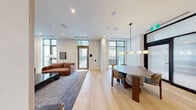 Located at 422 Cherry Street in Toronto's vibrant Canary District, this contemporary amenity space is thoughtfully designed to offer both comfort and style across a single level. The open layout seamlessly connects a dining area and a living room, creating a cohesive and functional environment suited for gathering and relaxation.

The dining area is anchored by a round marble-top table paired with upholstered chairs, illuminated by a modern globe pendant light fixture. Expansive floor-to-ceiling windows flood the space with natural light and frame views of an outdoor terrace complete with a pergola and seating area, accessible directly from the room.

The living room continues the refined aesthetic with warm terracotta-toned sofas arranged around a striking black terrazzo coffee table. Soaring ceilings and tall windows maintain an airy, open atmosphere, while direct access to an outdoor terrace — equipped with a barbecue — extends the usable living space outdoors.

Throughout, light hardwood flooring, crisp white walls, and recessed lighting contribute to a clean, modern palette. A kitchenette with dark countertops is also visible, adding a practical touch. The overall ambiance is polished yet inviting, reflecting a high standard of contemporary urban design.