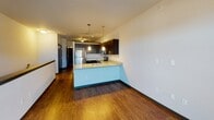 Located at 17589–17609 Dodd Blvd in Lakeville, MN, this single-floor unit offers a thoughtfully designed open-concept layout that seamlessly connects the kitchen and living areas. The kitchen is a standout feature, showcasing dark espresso cabinetry, granite countertops, and a full suite of stainless steel appliances including a refrigerator, electric range, microwave, and dishwasher. Pendant lighting hangs above the peninsula, adding a modern accent while providing functional task lighting. Rich hardwood-style flooring runs throughout the main living spaces, creating a warm and cohesive aesthetic. The open living area benefits from natural light streaming through a multi-pane window, complemented by a ceiling fan overhead. A half-wall peninsula defines the boundary between the kitchen and living space, offering additional seating or prep space. The bathroom continues the unit's consistent design language, featuring a granite-topped vanity with dark cabinetry, a dual-sink layout, and a large mirror with overhead lighting. An adjacent walk-in closet provides ample storage. Clean white walls and modern finishes throughout give the space a fresh, contemporary feel well-suited for everyday living in Lakeville.