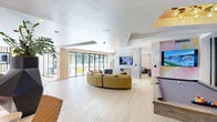 Located at 2700 Main St in Irvine, CA, this thoughtfully designed single-floor space offers a generous and open layout that blends contemporary style with eclectic, artistic flair. Light-toned hardwood flooring runs throughout, lending warmth and continuity to the entire floor plan.

The living area is the centerpiece of the space, anchored by a striking concrete feature wall that houses a built-in television above a sleek, modern fireplace. Adjacent to it, a dramatic hand-painted mural wall with soft, watercolor-inspired hues in pastel blues, pinks, and golds adds an artistic focal point that transitions beautifully into the surrounding rooms.

The open layout accommodates multiple seating arrangements, including a curved sectional sofa, a woven hanging chair, and a live-edge wood coffee table, all set against a textured, patterned accent wall with pendant lighting. A sculptural geometric planter with lush tropical foliage adds organic contrast to the modern interior.

A dedicated dining area sits adjacent, featuring a large rectangular table that opens directly to the outdoors through expansive floor-to-ceiling sliding glass doors. These doors flood the space with natural light and offer views of an outdoor courtyard, creating a seamless indoor-outdoor connection. The overall ambiance is sophisticated yet welcoming, balancing bold design choices with a bright, airy atmosphere.